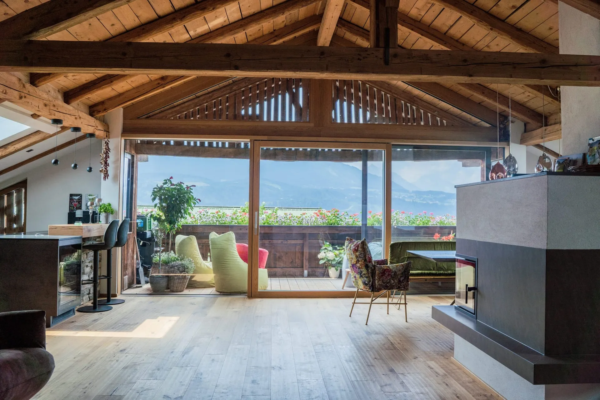 Dachgeschoss mit Holzbalken und großer Holz-Hebeschiebetür zum Balkon, dahinter die Berge