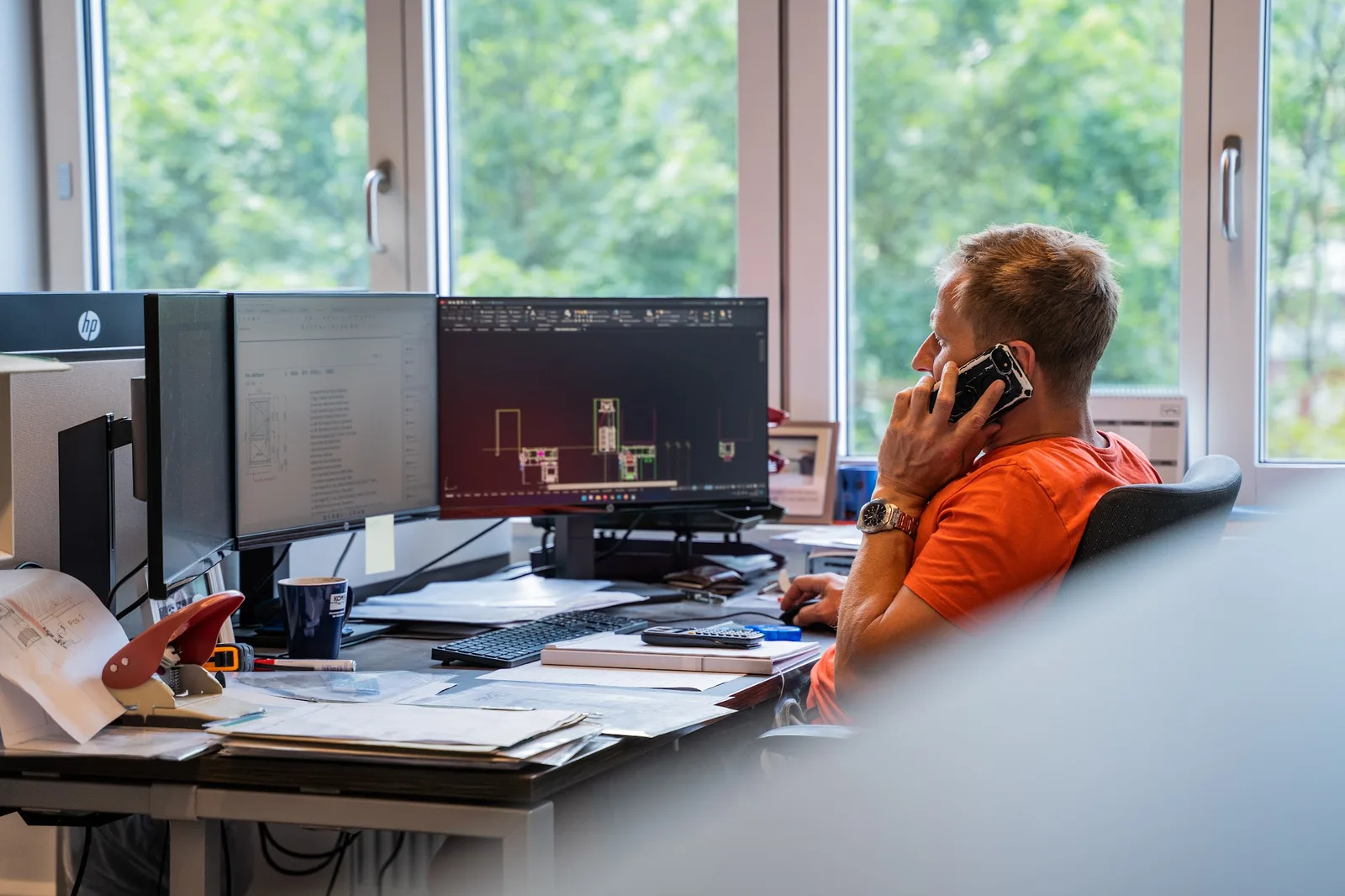 Mitarbeiter im Büro am Telefon, auf den Bildschirmen eine Planansicht