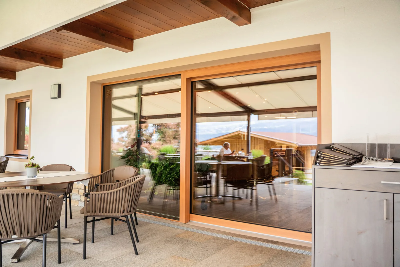 Holz-Hebeschiebetür zu einer überdachten Terrasse mit Tischen und Stühlen