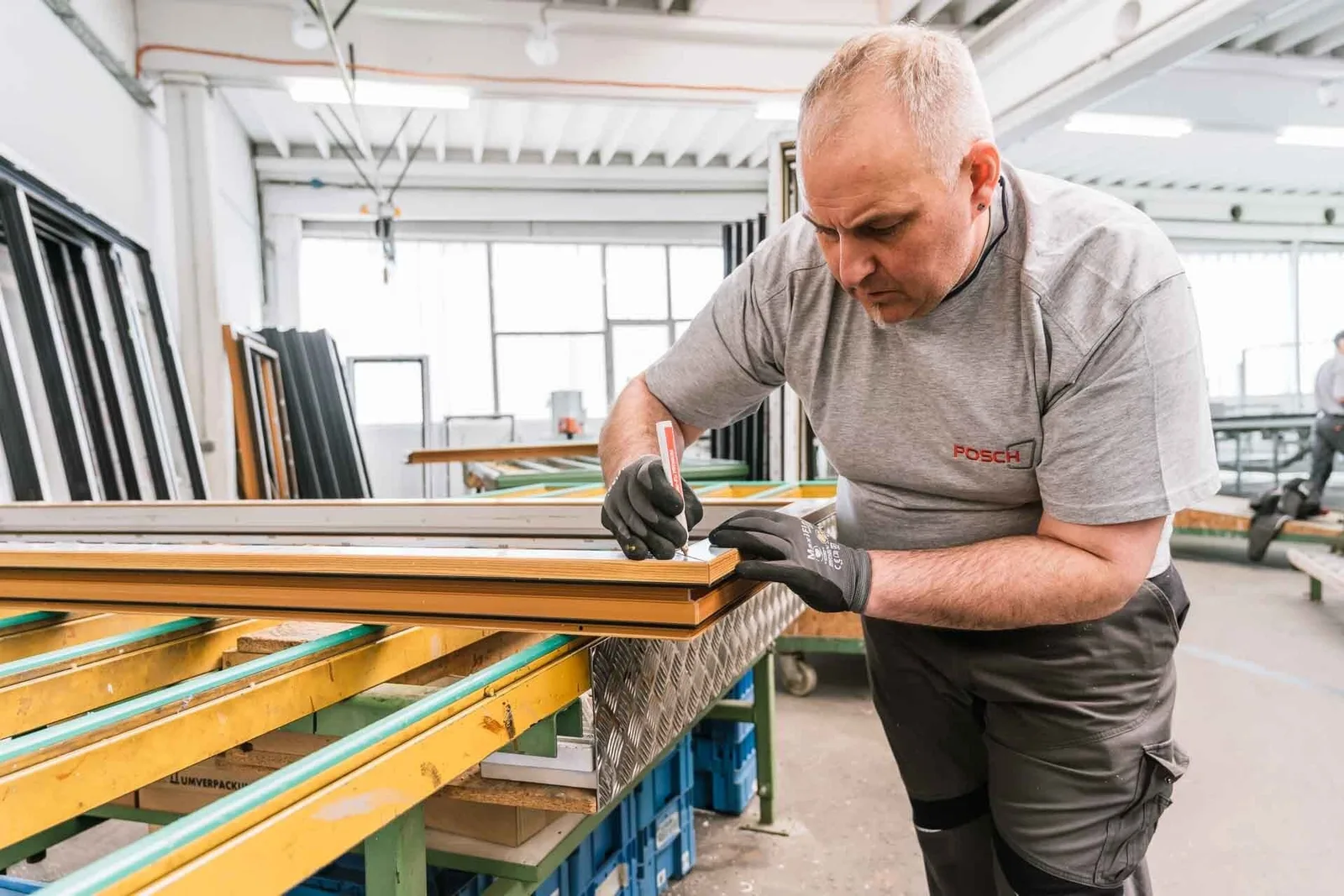 Mitarbeiter im POSCH-Shirt bearbeitet einen Fensterrahmen in der Produktionshalle